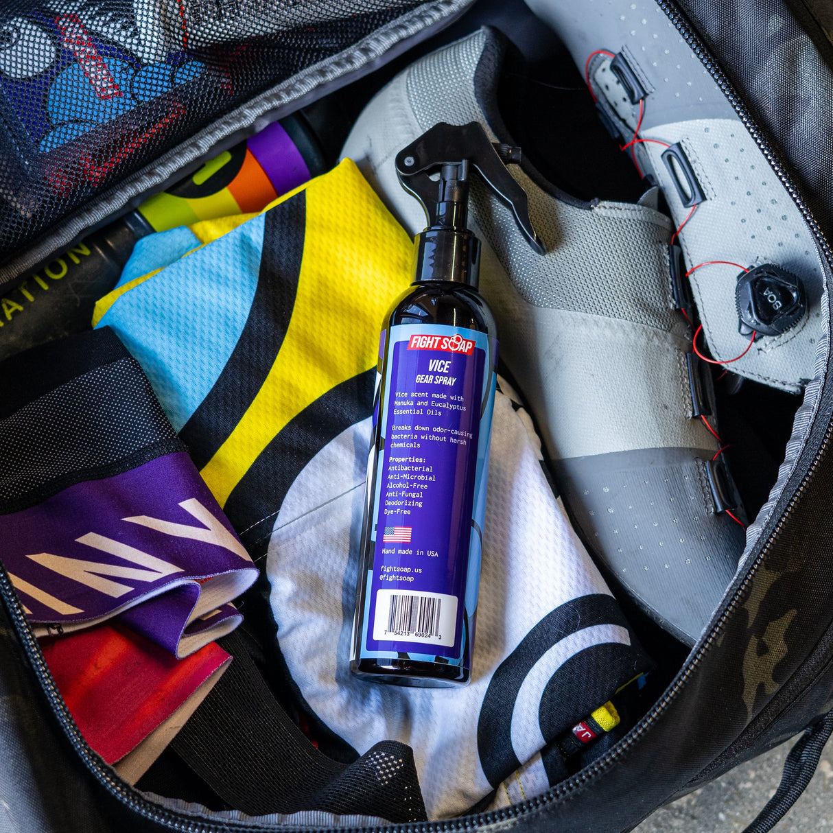 A black spray bottle labeled "Vice Gear Spray" with a trigger nozzle, placed inside a sports bag among athletic gear and accessories.