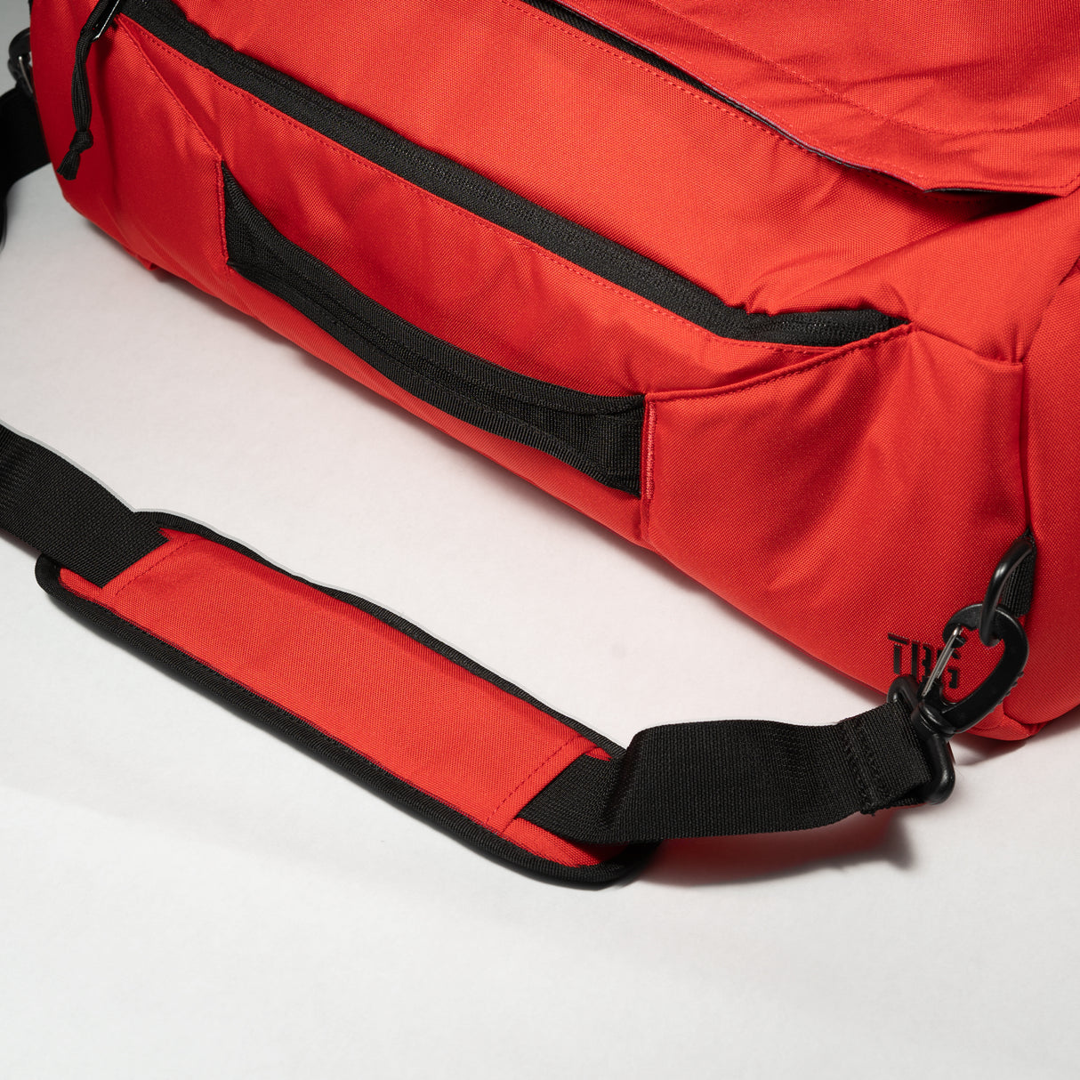 Red duffle bag with black zipper and strap, featuring a padded shoulder strap and a side pocket for storage.
