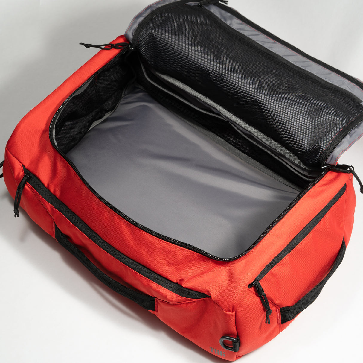 Red duffle bag with black zippers and interior mesh compartments, open to show spacious main storage area.