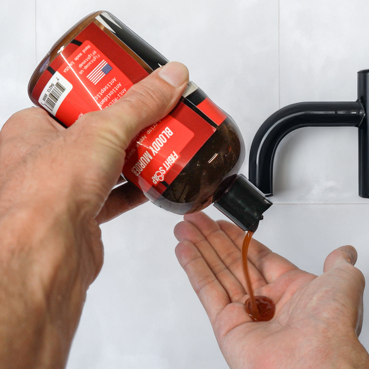 A person pouring Bloody Murder Body Wash from a brown bottle with a red label into their hand, with a black pump nearby.