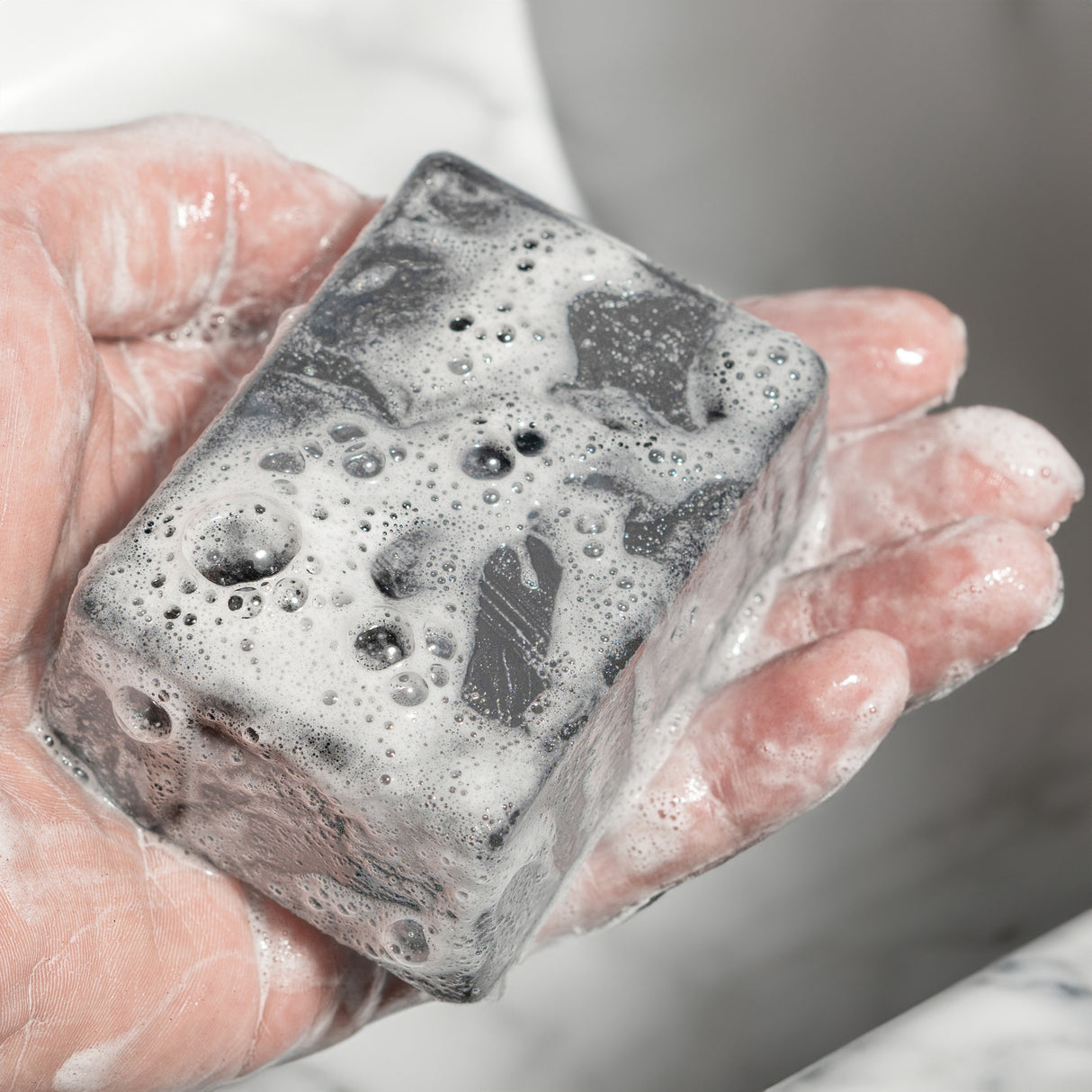 Hand holding a soapy, black WAR BAR soap with bubbles, ready for cleaning or washing.
