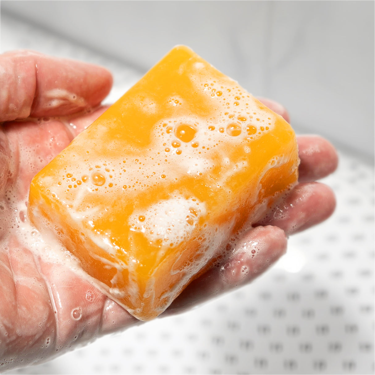 A hand holding a bar of soap labeled "Brazilian Bully," with a bright orange color and foamy lather on its surface.