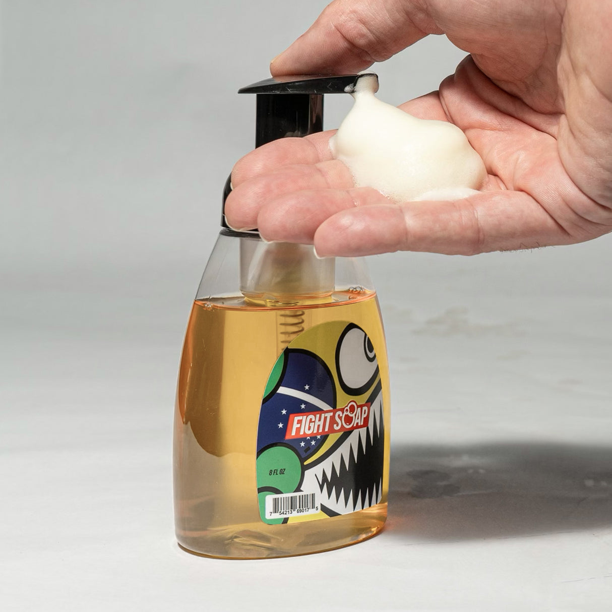 Hand pressing foaming Brazilian Bully Fight Soap onto a pump dispenser filled with liquid soap.