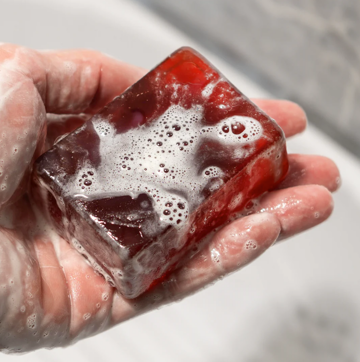 A hand holding a red soap bar labeled "TRIPLE THREAT," covered in soap suds and bubbles, with a blurred background.