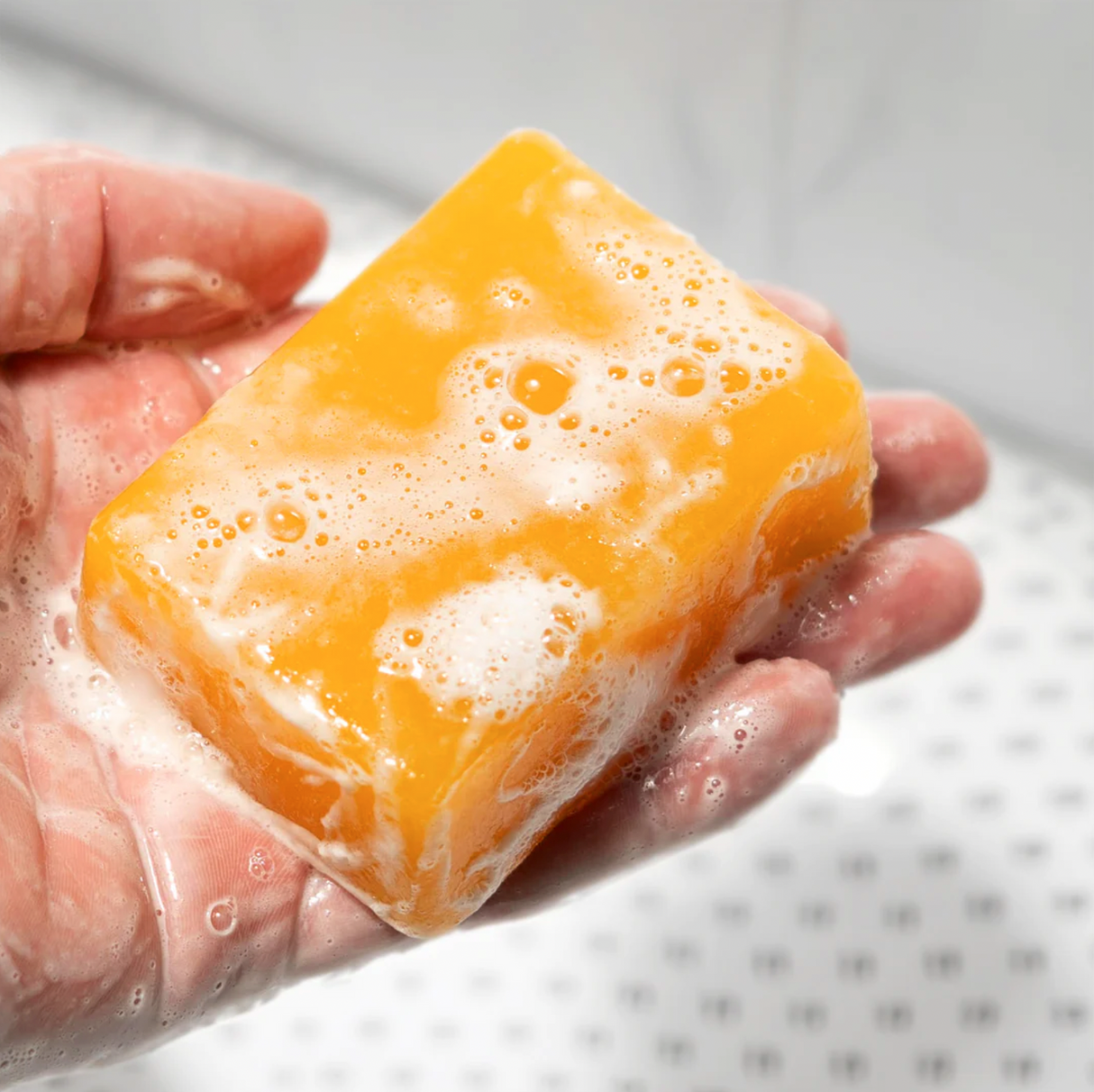A hand holding a bar of yellow soap with bubbles, labeled "TRIPLE THREAT," against a blurred background.