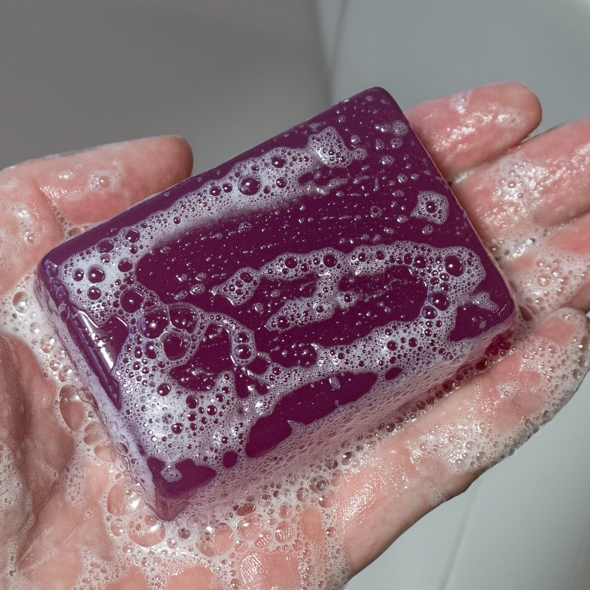 A hand holding a purple soap bar labeled "Zero Fucks Duck®," covered in soap suds and bubbles.