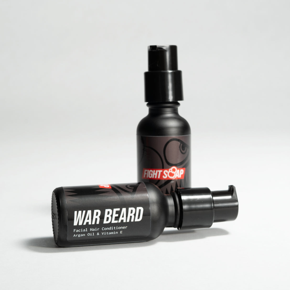 Two black bottles of WAR BEARD facial hair conditioner with argan oil and vitamin E, one lying down and one standing upright.
